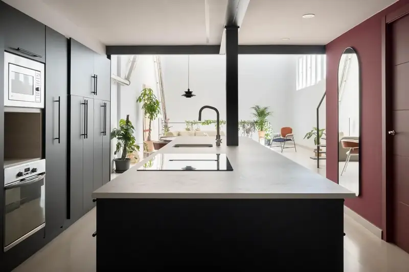 Cocina con isla central negra abierta al salón en un local reformado en Zaragoza